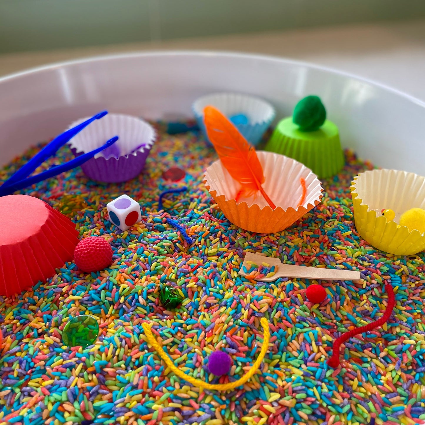 Colors Kit comes with dyed dry rice, colored baking cups, trinkets, tools, and accessories, as well as custom PlayMat and parent Sense of Help, all in our Play Pail.